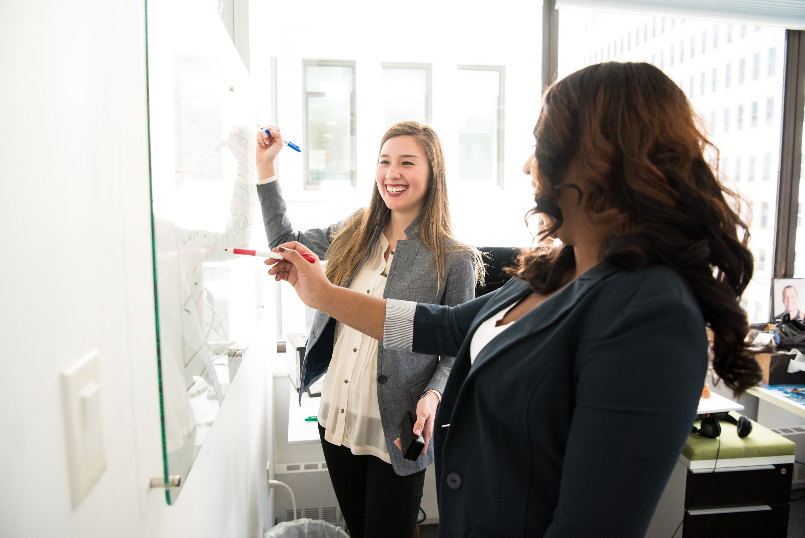 two people at a whiteboard writing and smiling talking about Effective Communication in International Businesses